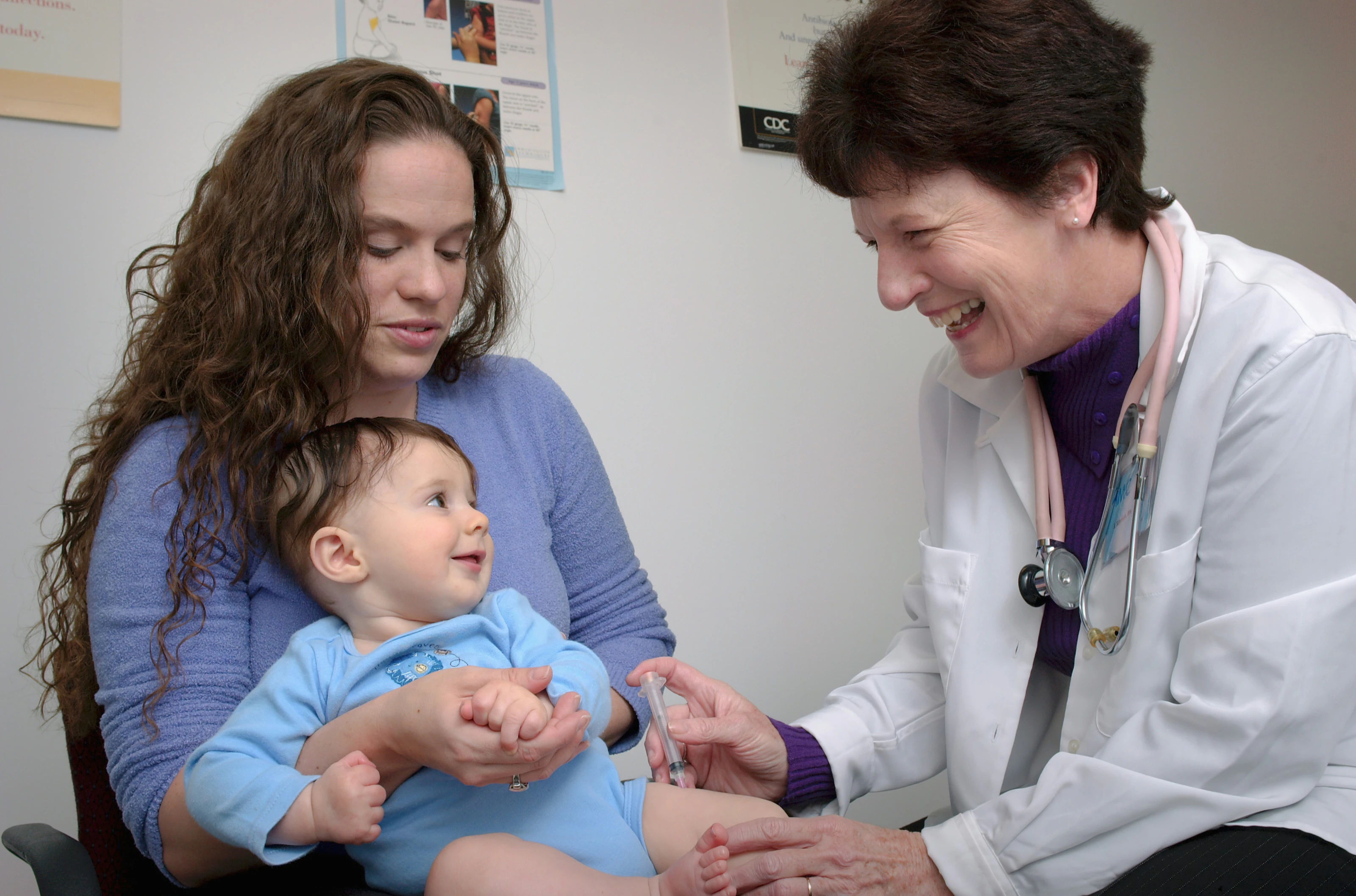 A pediatrician smiles at a baby on his mother’s lap during a checkup.